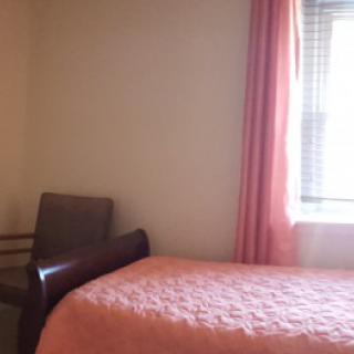 A minimalist bedroom with a bed, chair, and window with pink curtains.