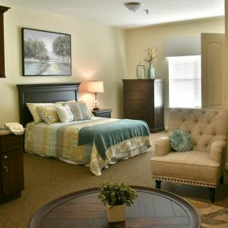 A cozy bedroom featuring a neatly made bed, an armchair, and warm lighting.
