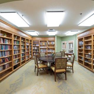 A cozy library room with wooden bookshelves, a round table, and chairs.