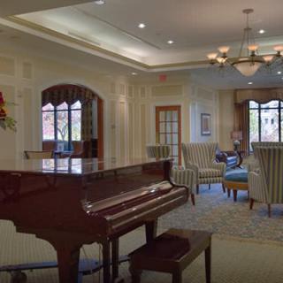 A cozy living room featuring a grand piano and elegant furnishings under a stylish chandelier.