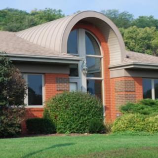 A suburban house with a brick exterior and large arched window, surrounded by lush greenery.