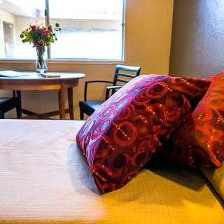 A cozy bedroom with vibrant pillows, a small table with chairs, and flowers by the window.