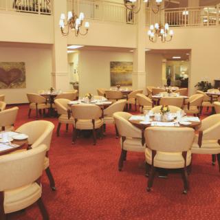 An elegant restaurant interior with round tables, cushioned chairs, and chandeliers.