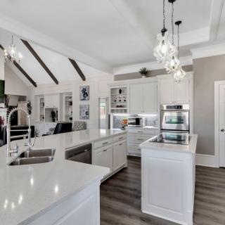 A modern kitchen with white cabinets and an island, featuring pendant lights and hardwood flooring in an open concept design.