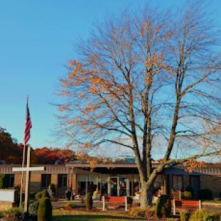 A serene view of a building with a prominent tree and an American flag, set against a clear autumn sky.