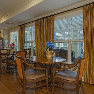 A cozy dining area with wooden tables, chairs, and large windows adorned with curtains.