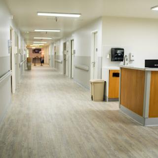 A well-lit corridor in a hospital, featuring a reception area and clean flooring.