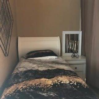 A cozy bedroom with a single bed and a nightstand featuring a mirror.