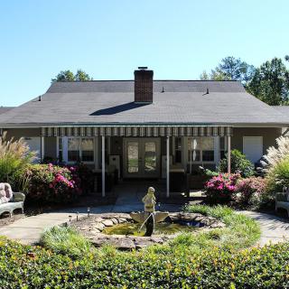A quaint house with a welcoming garden and fountain in the foreground.