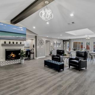 A modern living room with an open layout featuring a fireplace, a chandelier, and leather chairs on hardwood flooring.