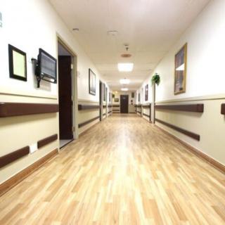 A well-lit corridor in a healthcare facility featuring wooden flooring and handrails along the walls.