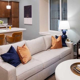 A modern living room with a comfortable sofa, colorful pillows, and a cozy lamp, adjacent to a kitchen area.