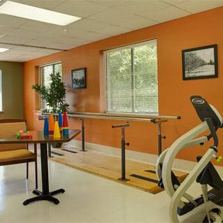 A rehabilitation room with exercise equipment, featuring parallel bars and a stationary bike.