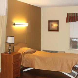 A serene bedroom setting featuring a single bed, bedside lamp, and warm lighting.
