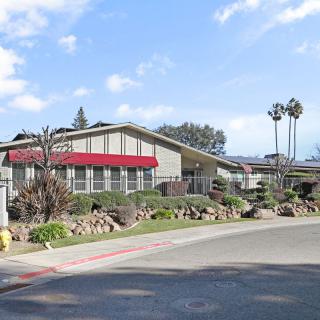 A mid-century modern building with a red awning surrounded by landscaped greenery and trees under a clear blue sky.