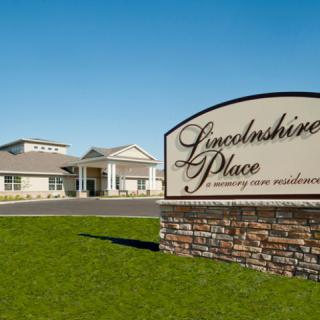 A view of Lincolnshire Place, a retirement home residence, with a prominent sign and manicured lawn on a sunny day.