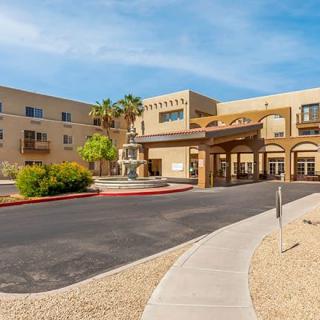A modern hotel entrance with palm trees, set in a desert-like landscape.