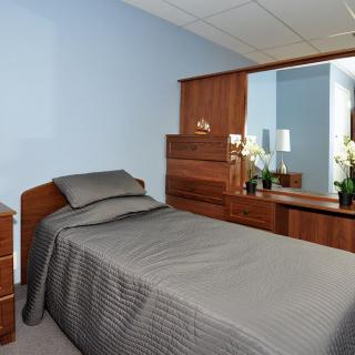 A neatly arranged bedroom with a single bed and modern wooden furniture.