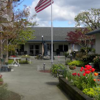 A charming courtyard with a garden blooming with colorful flowers, featuring a building in the background and an American flag flying high.