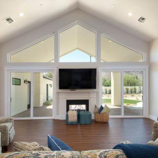 A spacious living room with a vaulted ceiling and large windows, featuring a central fireplace and television.