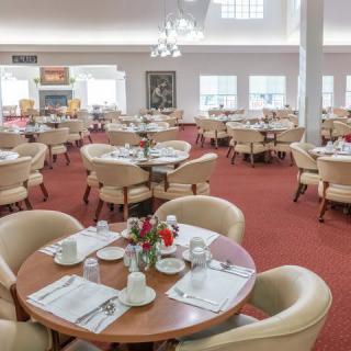 A spacious dining area with neatly arranged tables and chairs on a red carpet.