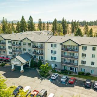 Aerial view of a residential apartment building with a parking lot in front, surrounded by trees and greenery.