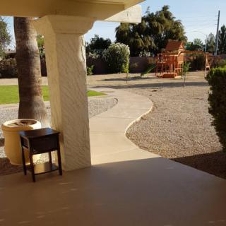 A sunny backyard viewed from a patio, featuring a pathway and garden furniture.