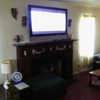 A cozy living room featuring a TV mounted above a fireplace with surrounding decor and furniture.