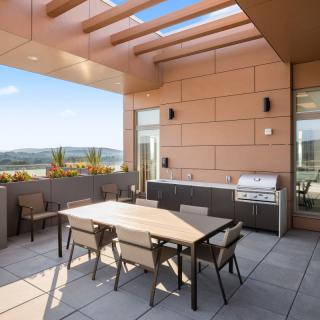 A modern outdoor patio with a dining set and grill, featuring scenic views.