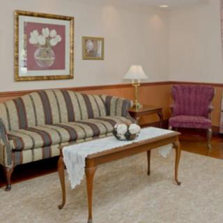 A cozy living room with a striped couch, an armchair, and a classic coffee table accented by elegant wall art and a lamp.