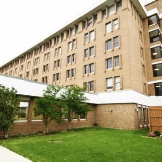 A multi-story residential building with a well-maintained lawn and trees.