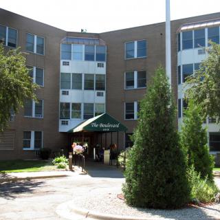 A multi-story residential building with a main entrance surrounded by greenery.