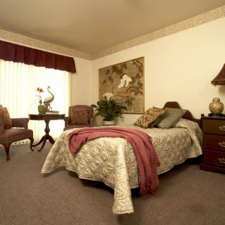 A cozy bedroom with classic decor, featuring a bed, armchairs, and a side table.