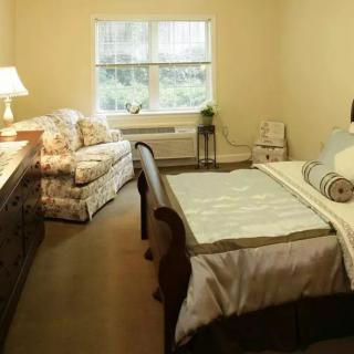 A cozy bedroom featuring a bed, sofa, and lamp by the window.