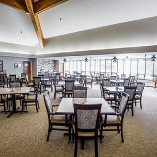 A spacious dining area featuring multiple tables and chairs, well-lit and with large windows offering a view outside.