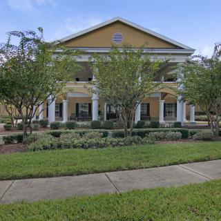 A large, two-story yellow building with columns, surrounded by a well-maintained garden and lawn.