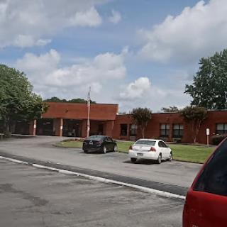 A view of a red brick building with a parking lot under a partly cloudy sky.