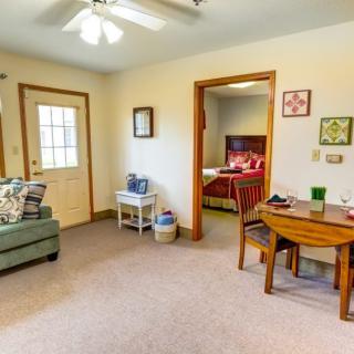 A cozy living space with a view into a bedroom, featuring a sofa, small table with chairs, and decorative elements.