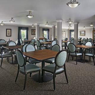 An empty dining room with neatly arranged tables and chairs, featuring ceiling fans and soft lighting.