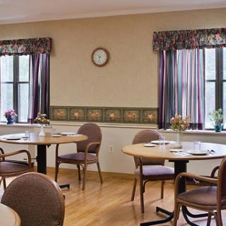 A cozy dining room setup with wooden tables and chairs, featuring large windows adorned with curtains.