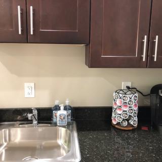 A kitchen countertop with a sink, soap dispenser, coffee maker, and cabinets above.