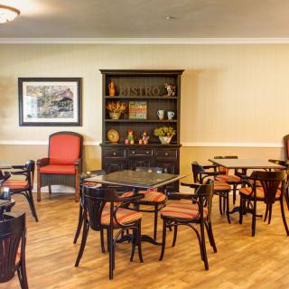 A cozy dining area featuring tables, chairs, and a shelving unit against a wood-floored interior.