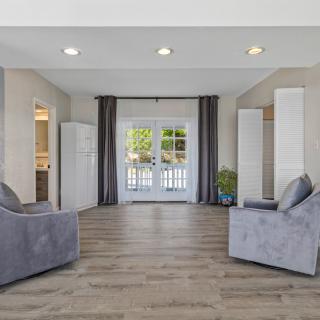 A modern living room with two gray sofas, hardwood flooring, and ample natural light.