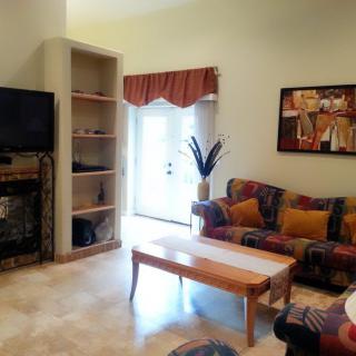 A cozy living room with a sofa, coffee table, and wall-mounted television, complemented by artwork and decorative shelves.