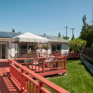 A sunny backyard with a wooden deck, patio furniture, and an umbrella.