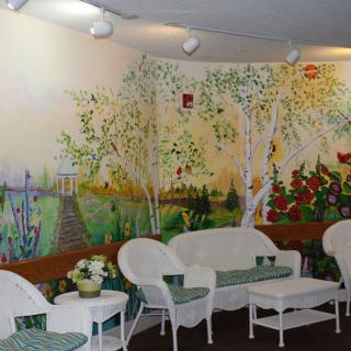 A cozy seating area with white wicker furniture set against a vibrant mural depicting a nature scene.