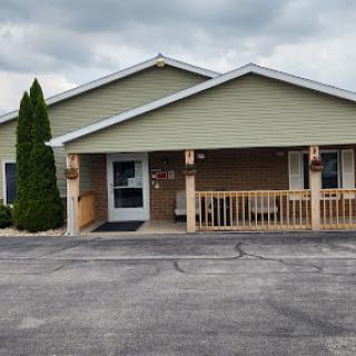 A welcoming single-story building with a covered entrance and green accents, set against a cloudy sky.