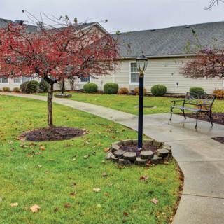 A residential garden scene with autumn trees, a pathway, benches, and a lamp post.