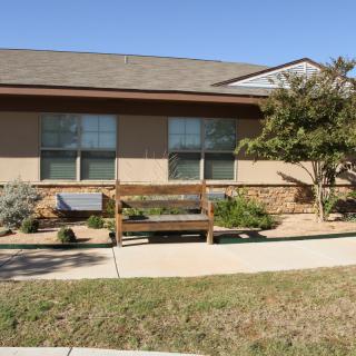 A small house with a bench in front and landscaped garden.