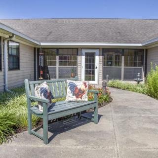 An inviting outdoor space featuring a bench with pillows along a pathway leading to a house with a screened porch.
